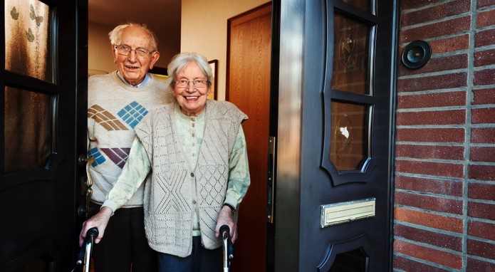 Ein Seniorenpaar steht zusammen in der geöffneten Türe zu ihrem Haus.