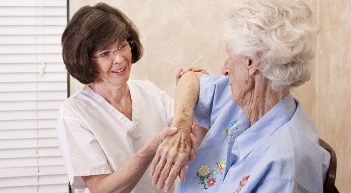 Eine Pflegerin unterstützt eine ältere Frau mit weißen Haaren bei leichter Gymnastik mit dem Arm.
