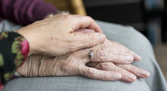 Eine Hand liegt auf den beiden Händen einer älteren Frau.