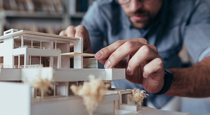 Ein Mann bastelt an einem Modell eines Wohnhausneubaus.