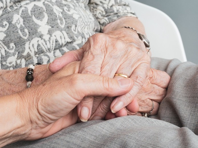 Eine Hand hält fürsorglich die beiden auf dem Schoß liegenden Hände einer älteren Faru