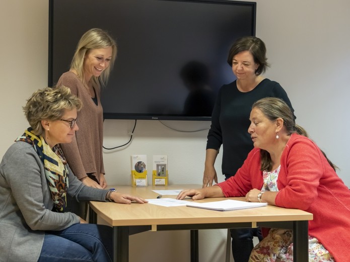 Die Mitarbeiterinnen des Pflegestützpunkts im Landkreis Schwäbisch Hall sitzen und stehen um den Tisch im Beratungsraum herum. Von links nach rechts: Silvia Haase, Carina Kohler, Dorothee Schumm und Regine Hammer.